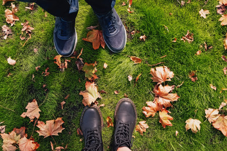 Male and female feet standing on the green grass with dry autumn leaves