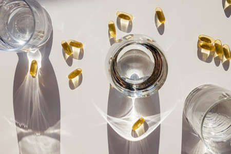 Omega 3 capsules and glasses with water on white table.の写真素材