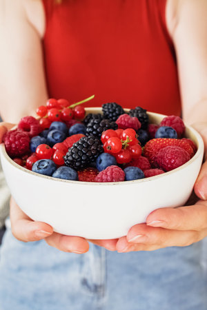 Female hands holding a bowl of delicious summer berriesの写真素材