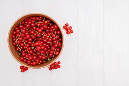 Red currant in a bowl on white wooden tableの写真素材