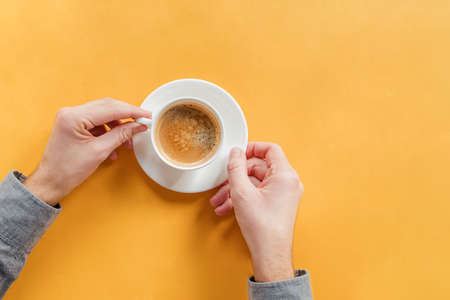 Mans hands holding a cup of coffee on yellow tableの写真素材