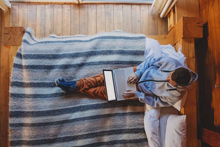 Man working on laptop sitting on cozy bedの写真素材