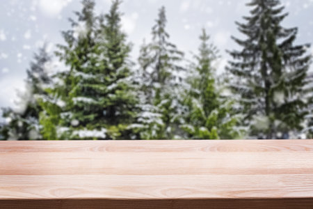 Empty woooden table top with blurred spruce trees on the background.