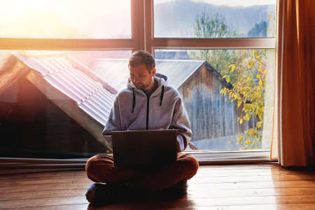 Man using laptop sitting on the floor near big windowの写真素材