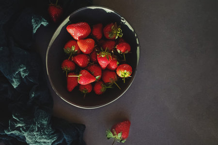 Fresh organic strawberries in a bowl on a stone table, top view. Dark and moody toned photo, low...