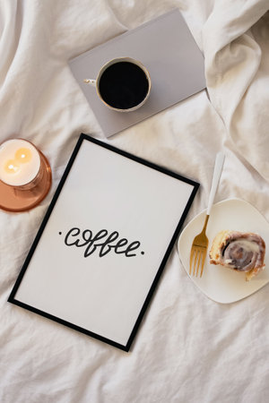 Lifestyle flat lay with cup of coffee, candle and poster with text Coffee on white bedの写真素材