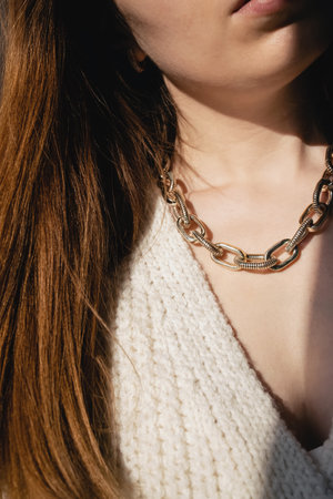 Close-up young woman in white sweater wearing golden chain necklace.の写真素材