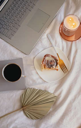 Composition with cinnamon bun, coffee, burning candle and laptop on the bed.の写真素材