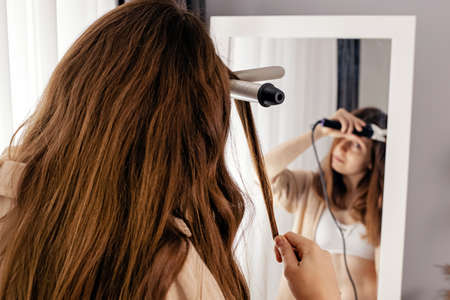 Young woman styling her shiny long brown hairの写真素材