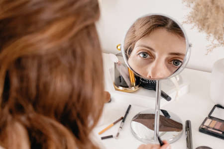 Young woman applying make-up to her face, looking at the round mirrorの写真素材