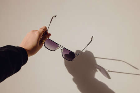 Female hand holding sunglasses over the white wall.の写真素材