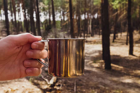 Mans hand holding stainless steel mug with hot tea close-up.の写真素材
