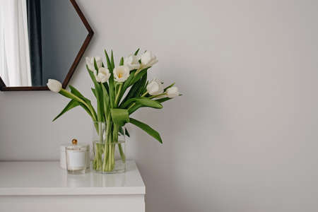 White tulips in a glass vase on a white chest of drawers.の写真素材