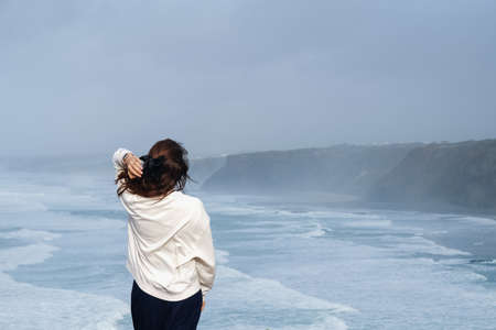 View from the back of woman standing on a shore with a view to stormy Atlantic oceanの写真素材