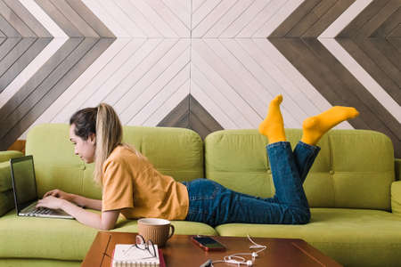 Young woman lying on the couch with her laptopの写真素材