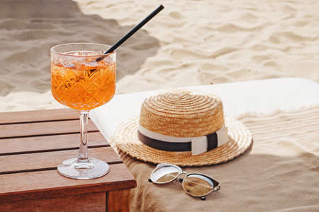 A glass of aperol Spritz , straw hat and sunglasses on the beachの写真素材