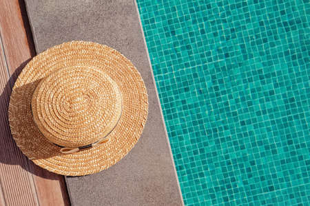 Womans straw hat lying on the edge of the swimming pool with turquoise waterの写真素材