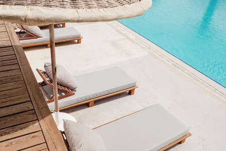 Wooden sunbeds with ratang umbrellas near swimming poolの写真素材