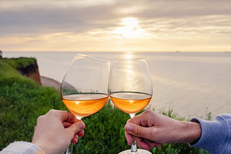 Couple clinking with two glasses of rose wine on sunset with a view to the sea.
