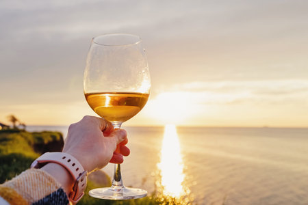 Woman hand holding a glass of rose wine at sunsetの写真素材