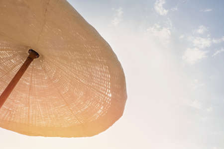 Large beach umbrella of wicker and cloth in natural colors on the blue sky backgroundの写真素材