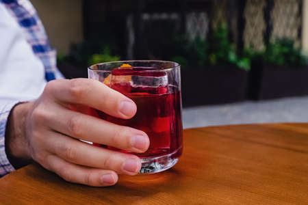 Close-up of male hand holding a glass of alcohol cocktail of red color.の写真素材