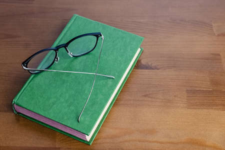 Reading glasses on the book with hard cover on the wooden tableの写真素材