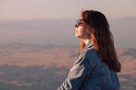Woman in denim jacket enjoying warm weather with a view on the hillsの写真素材