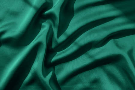 Emerald green tone satin fabric with folds in natural sunlightの写真素材