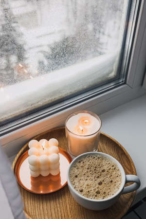 Cozy atmosphere winter still life with hot drink and candles on the windowsill, with snow on the background.の写真素材