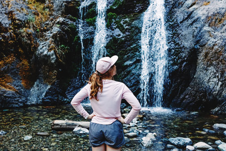 Young woman enjoying time near the waterfall after the hike, view from the back