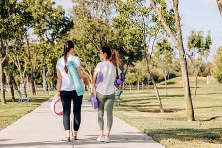 Two young women walking in the morning park, going to exercise outdoors. Carrying mats and other equipment for yoga.の写真素材