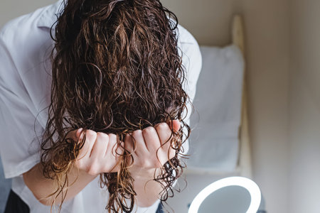 Woman scrunching her hair to form curls. Applying curly method for hair styling