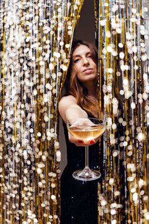 New Year's eve party concept. Woman holding a glass of champagne, festive shiny decor and blurred lightsの写真素材