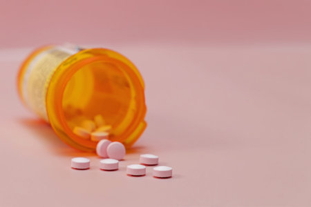 Pills in plastic orange bottle close-up, prescribed medication on pink background. Selective focus.