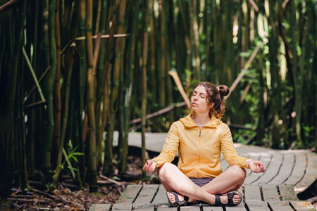 Young woman sitting in meditation pose, relaxing among the bamboo tress.の写真素材