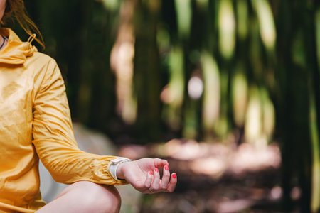 Close-up of the hand of woman relaxing in lotus pose in the park. Blurred green trees on the backgroundの写真素材