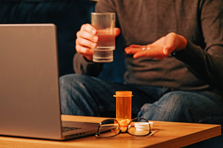 Unrecognizable man taking medicine while working at the laptop. Pain relief, headache