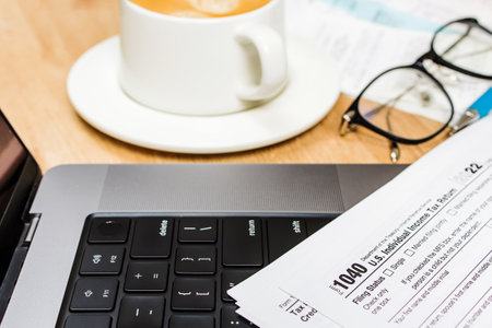 Laptop, coffee, pen and US individual tax form on the desk. Filling taxes, selective focusの写真素材