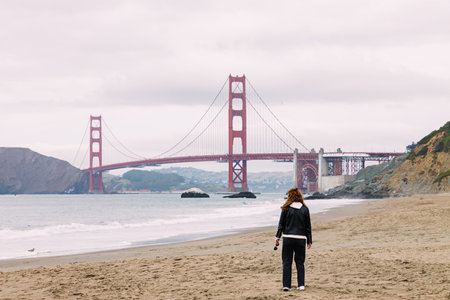 Woman walking on the beach with a view to Golden Gate Bridge, San Francisco, California. Cloudy foggy dayの写真素材
