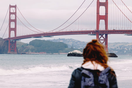 Woman looking on the Golden gate bridge, selective focus on the bridge, cloudy day in San Francisco,...