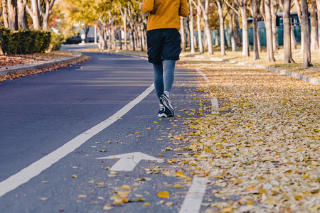 Feet of unrecognizable man jogging outdoors in the fall. Yellow leaves on the street, autumn runningの写真素材