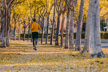 Man jogging at fall. Running on the street with lots of yellow leaves on the ground, view from the backの写真素材