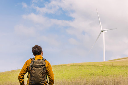 Man looking on the wind power mill among green hillsの写真素材