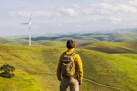 Man looking on the wind power mill among green hills, view from the backの写真素材