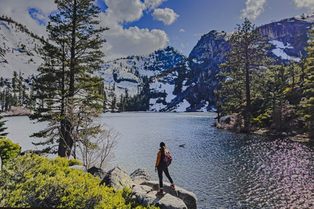 Woman standing near small peaceful lake with snowy mountains on the background, hiking with a backpackの写真素材
