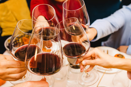 Hands clinking with a glasses filled with red wine sitting at the Thanksgiving dinner table. Celebration, gather, Friendsgivingの写真素材