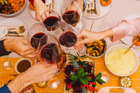 Unrecognizable people clinking with a glasses filled with red wine sitting at the Thanksgiving...