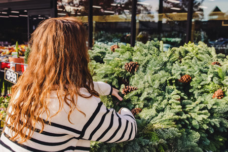 Woman choosing a decorative Christmas wreath to buy at outdoor store or marketの写真素材