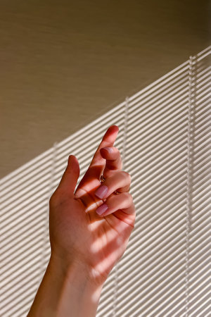 Female hand with pink nail polish in natural sunlight with shadows from blindsの写真素材